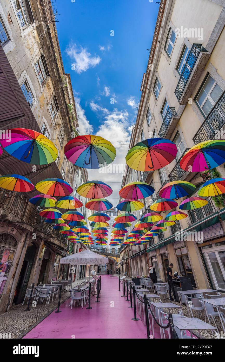 Lissabon, Portugal. 13. November 2023: Rosa Straße (Rua Nova do Carvalho) mit farbenfrohen Regenbogenschirmen, die zwischen Gebäuden hängen Stockfoto