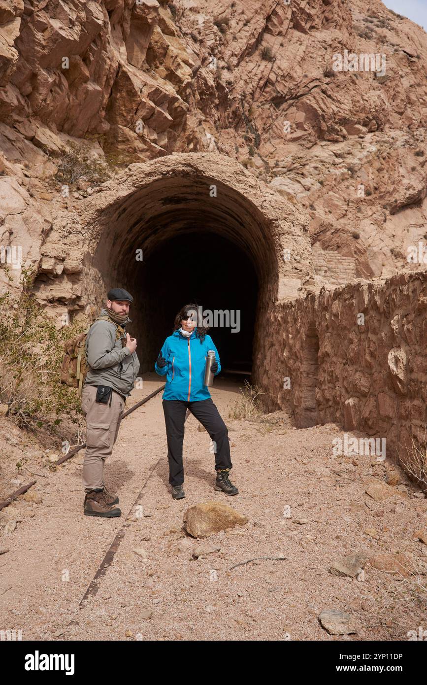 Ein paar Freunde, Mann und Frau, laufen auf den Gleisen in einer bergigen Gegend von Potrerillos, Mendoza, Argentinien. Hinter ihnen befindet sich ein Tunnel. Stockfoto