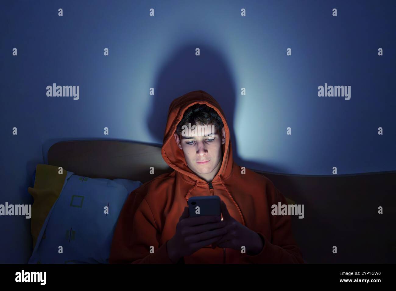 Teenager, der spät nachts im Bett ein Mobiltelefon benutzt, beleuchtet durch Bildschirmbeleuchtung Stockfoto