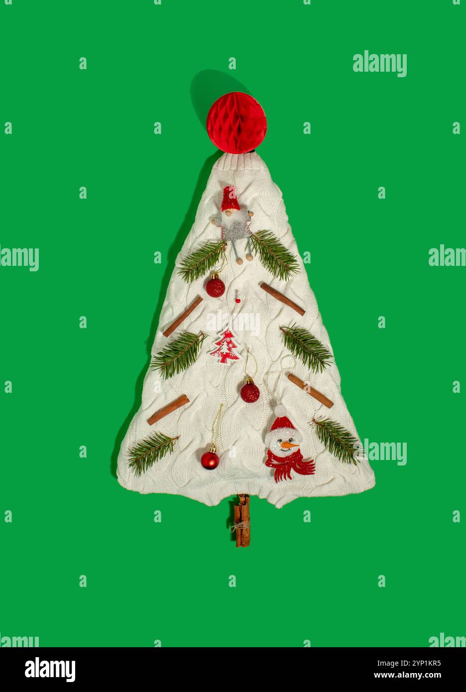 Weihnachtsbaum aus strukturiertem weißem Pullover mit roten Weihnachtsschmuck und grünen Zweigen Stockfoto