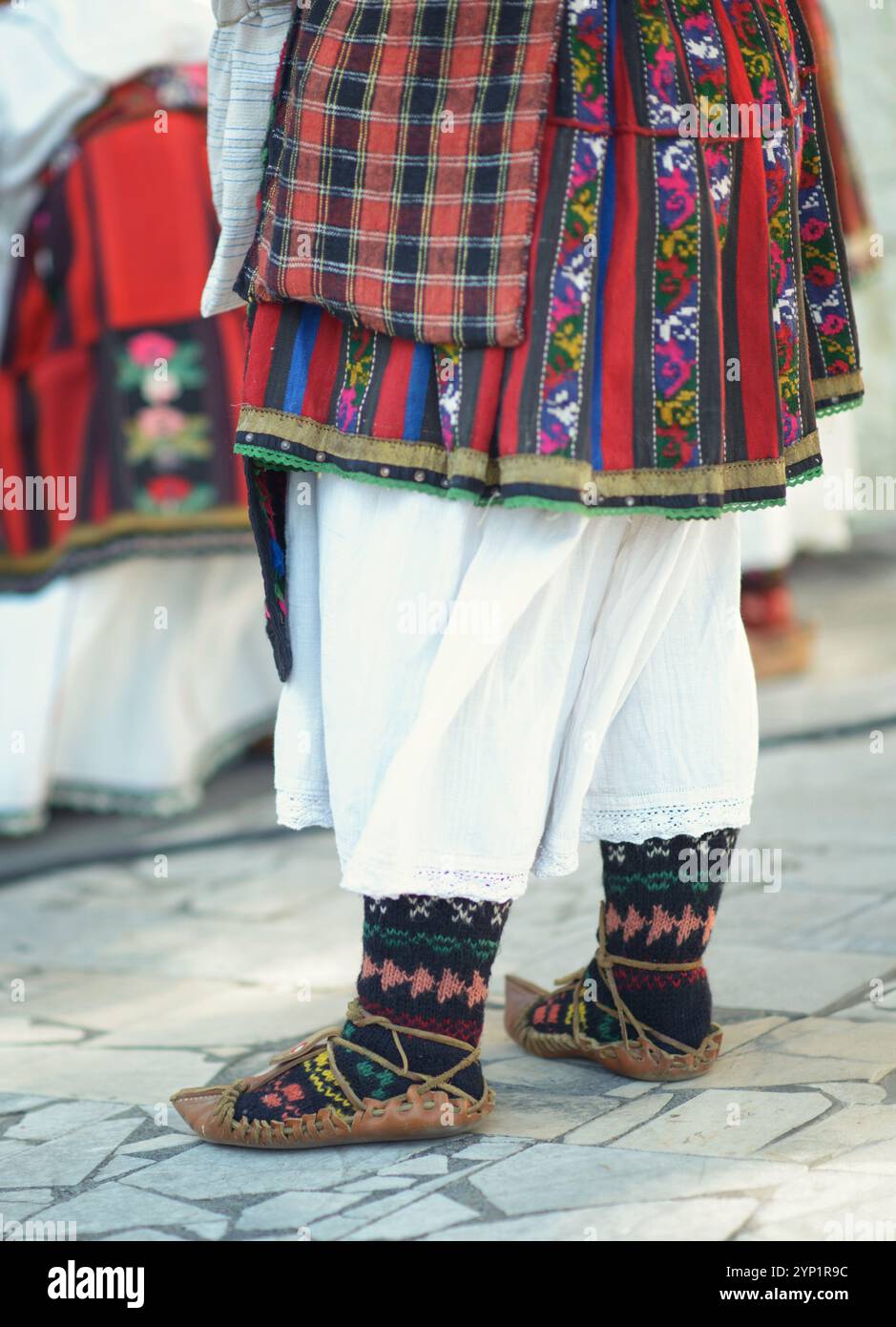 Komplizierte bulgarische Kleidung mit handgefertigter Umhängetasche, farbenfroher besticktem Rock, weißem Unterrock, gemusterten Socken und traditioneller Tradition Stockfoto
