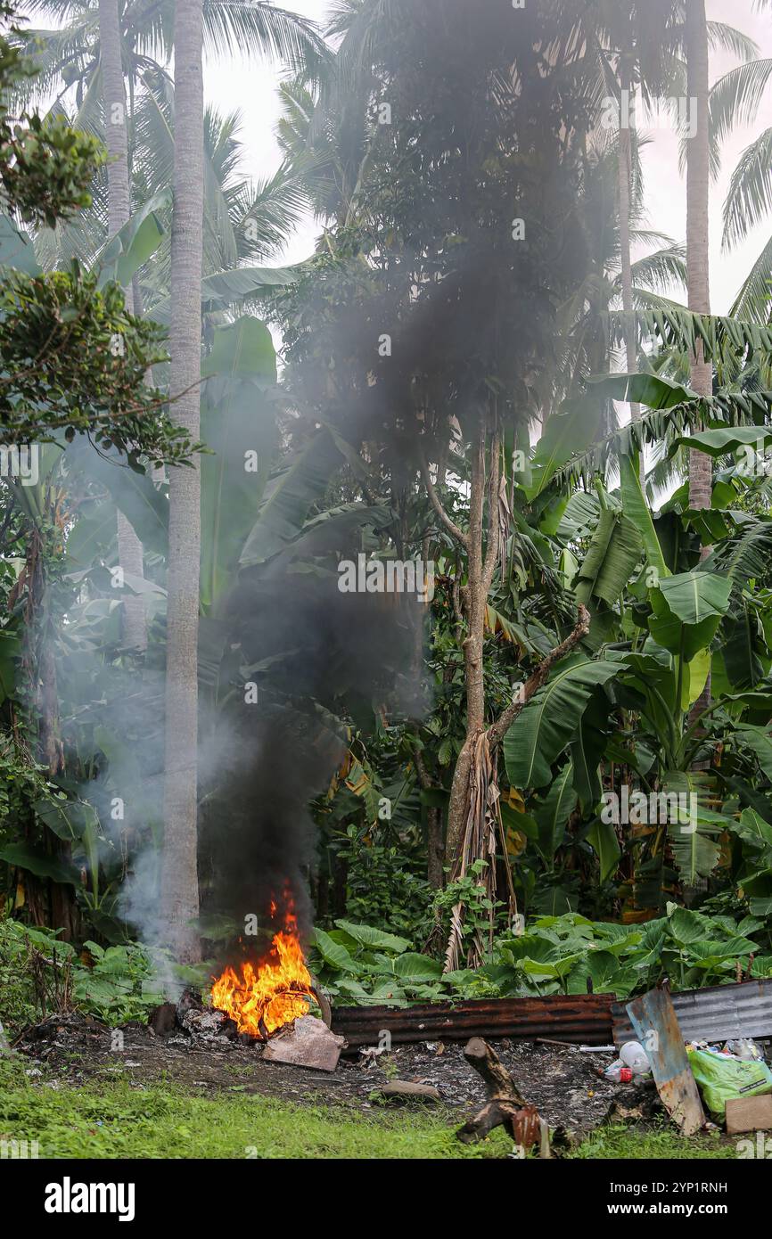 Laguna, Philippinen. 28. November 2024: Müllfeuer am Rande eines Waldes. Viele Filipinos verbrennen Müll in Hinterhöfen, eine häufige Ursache für Fehden in der Nachbarschaft. Das Gesetz verbietet offenes Abbrennen, aber diese umweltschädliche und schädliche Praxis namens „Pagsisiga“ ist in ländlichen Gebieten weit verbreitet. Dämpfe und Verbrennungsrückstände von Haushaltsabfällen, Elektronik, Kunststoff, Synthetik, Chemie, Pappe, organische Materialien verschmutzen Umwelt, Grundwasser und Luft. Die fünfte Sitzung des zwischenstaatlichen Verhandlungsausschusses für Kunststoffverschmutzung (INC-5) findet diese Woche in Südkorea statt. Quelle: Kevin Izorce/Alamy Live News Stockfoto