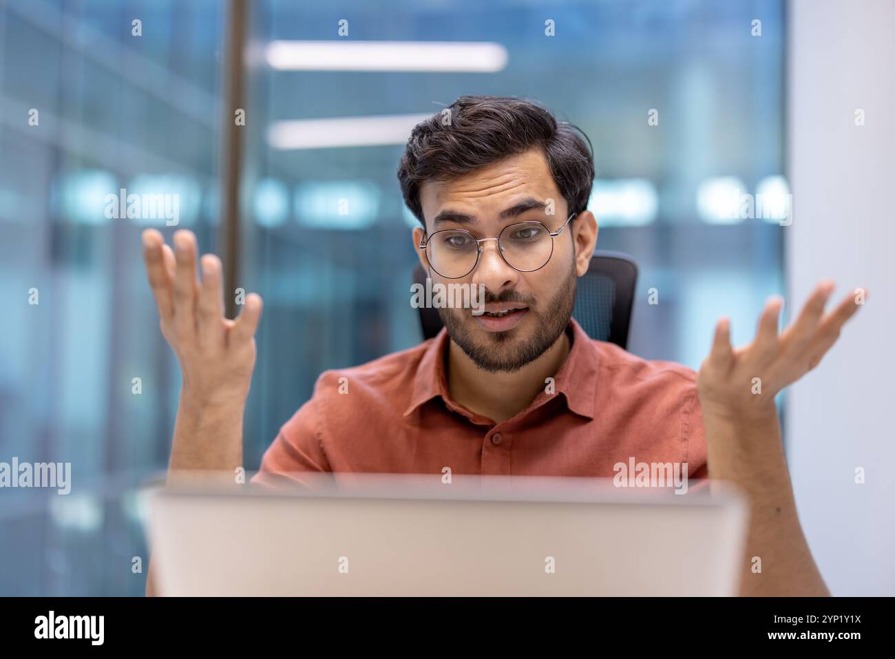 Junger Profi in lässigem Hemd, der sich an Online-Videoanrufen beteiligt und Begeisterung und Neugier zum Ausdruck bringt. Konzeptualisiert Kommunikation und Arbeitsdynamik in modernen Geschäftsumgebungen. Stockfoto