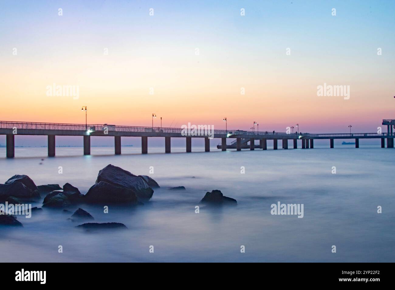 Sonnenaufgang über dem Meer in einer geheimnisvollen felsigen Bucht mit einem Kai im Hintergrund Stockfoto