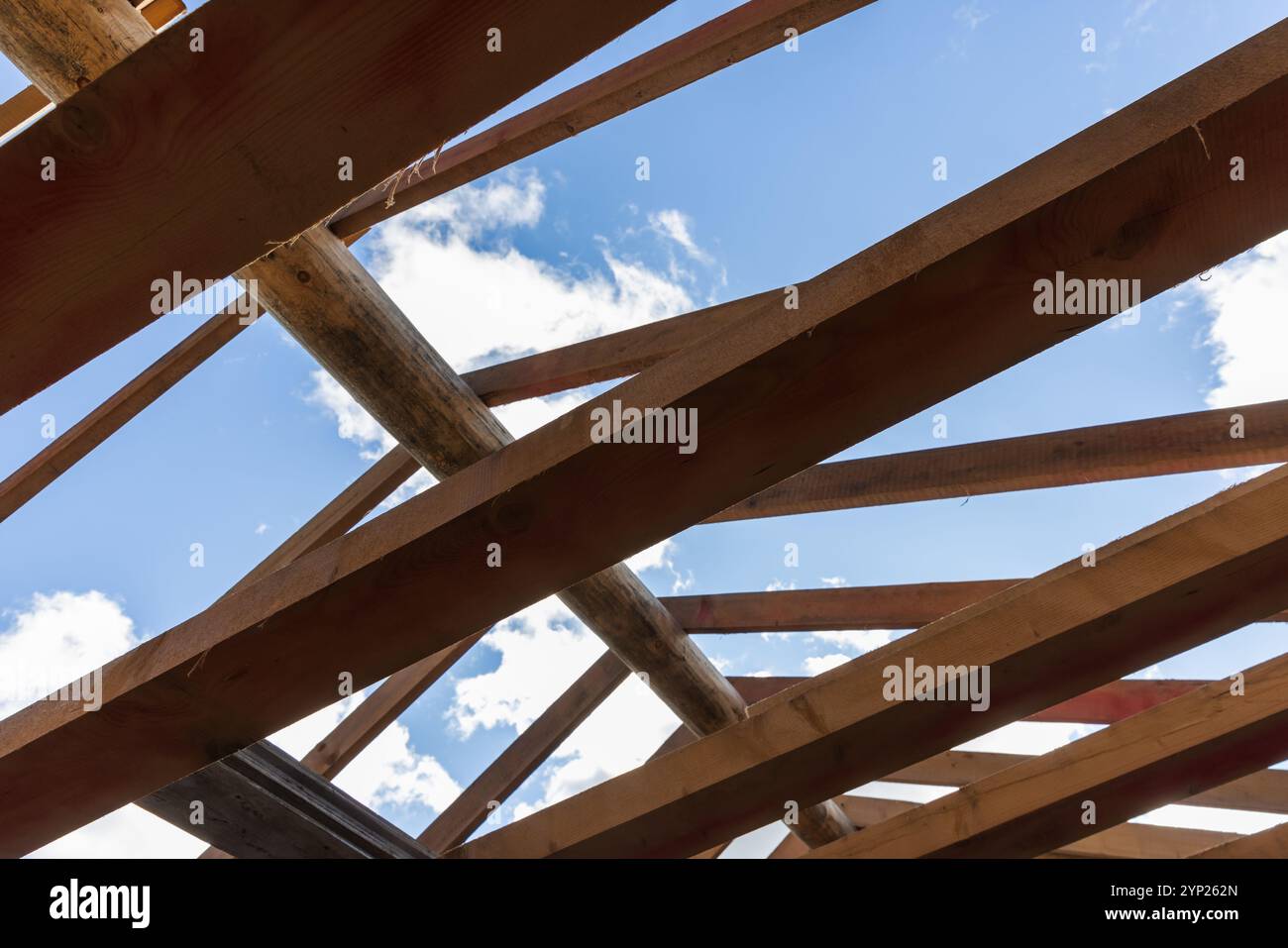 Unvollendetes Dach eines Blockhauses im Bau. Ungefärbte natürliche Kiefernbäume und Bretter sind unter hellblauem Himmel, Hintergrundfoto Stockfoto