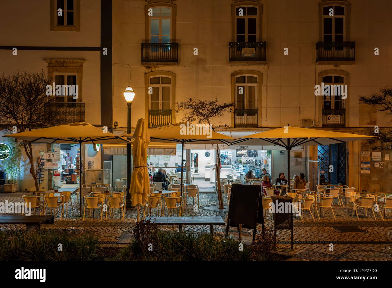 Straßencafés am Abend auf dem mit Kopfsteinpflaster gepflasterten Hauptplatz (Praca da República), Tavira, Algarve, Portugal Stockfoto