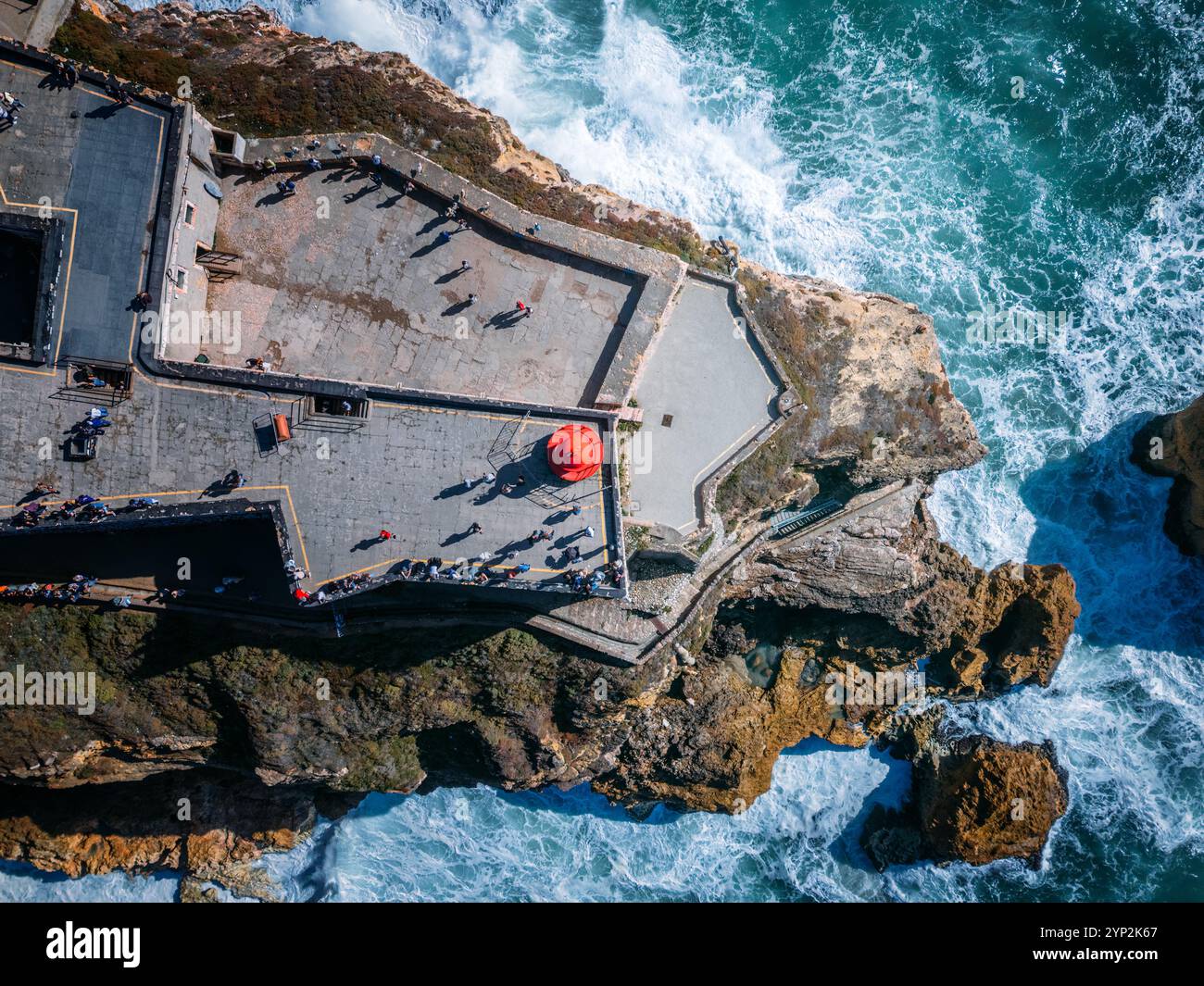 Luftdrohne von oben nach unten auf den Nazare-Leuchtturm mit Wellen, die auf Felsen darunter stürzen, Nazare, Oeste, Estremadura, Portugal, Europa Stockfoto