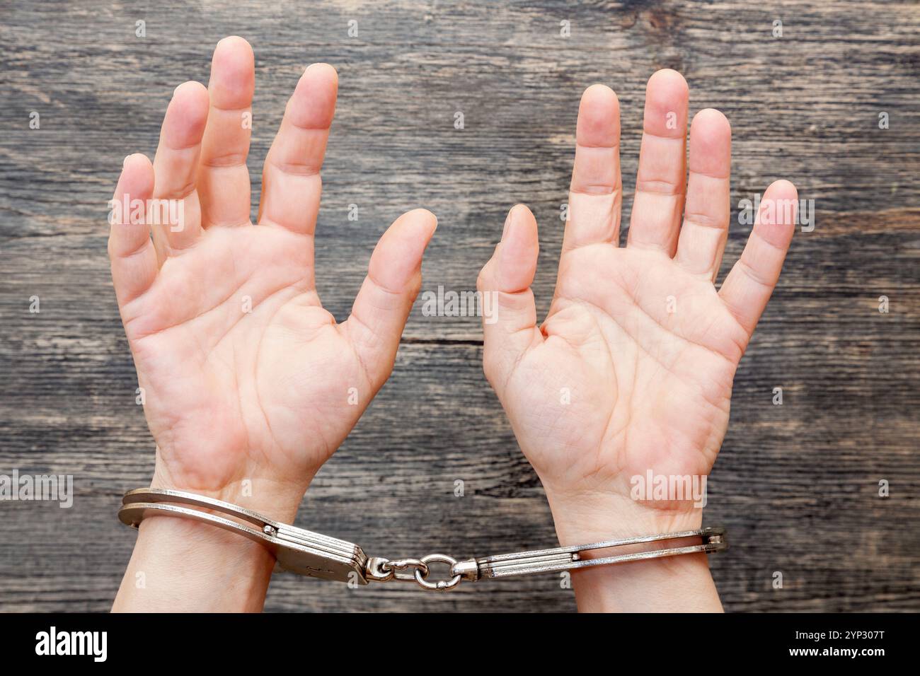 Hände mit Handschellen auf einem grauen hölzernen Hintergrund. Stockfoto