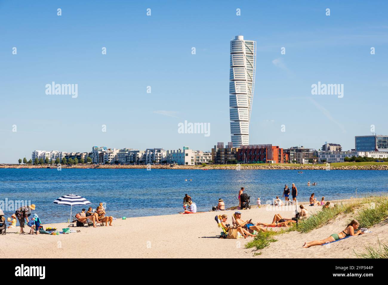 Menschen, Paare und Familien mit Kindern genießen Sonnenbaden am Strand von Ribersborg in Malmö, Schweden, mit Blick auf den sich drehenden Torso-Turm. Stockfoto