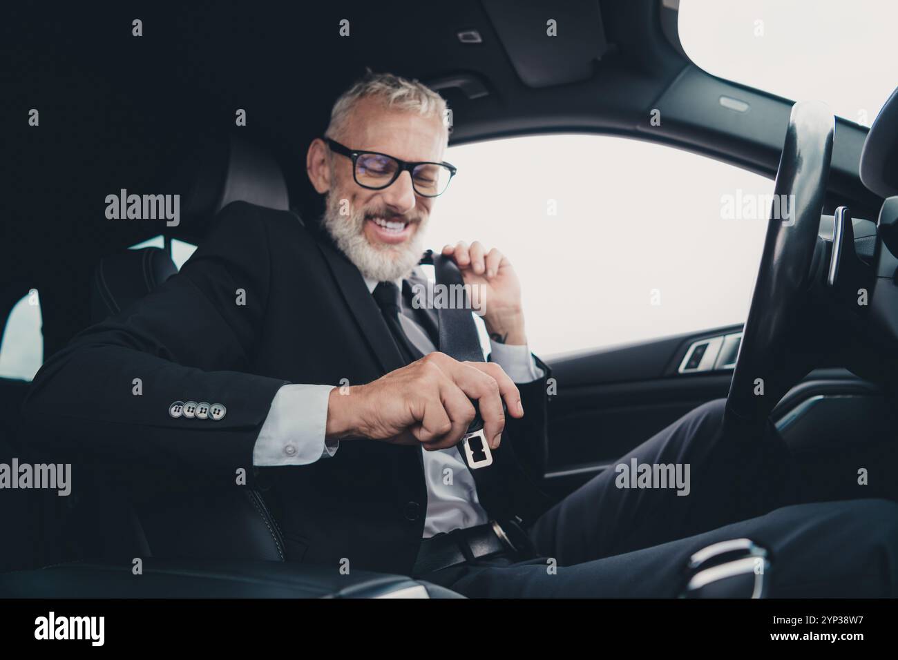 Ein reifer Geschäftsmann passt den Sicherheitsgurt des Autos an, während er sich auf die Fahrt vorbereitet, und stellt Reise- und Geschäftskonzepte in formalwear vor Stockfoto