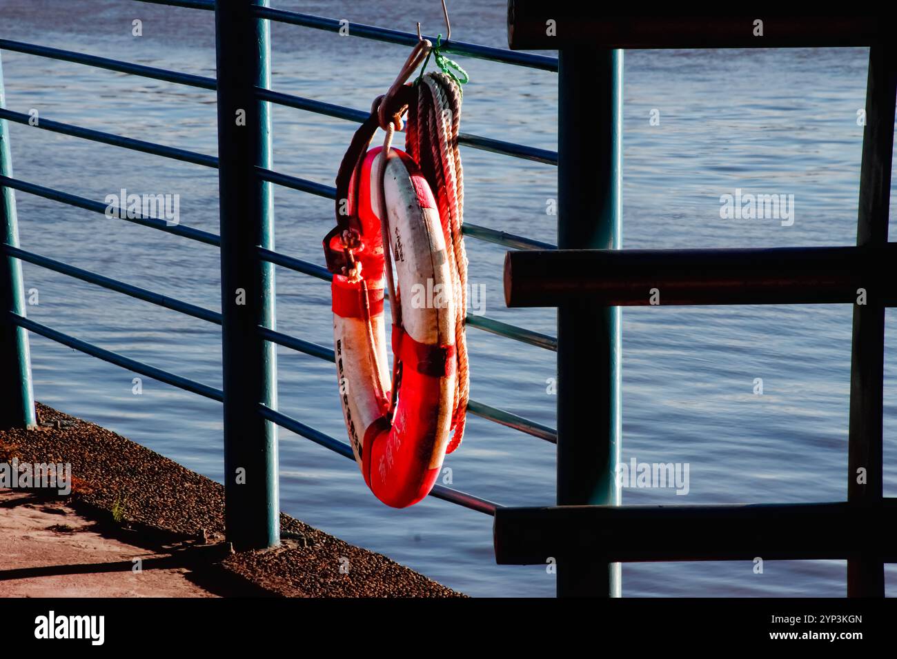 Ein leuchtend rot-weißer Rettungsschirm hängt an einem Metallgeländer mit Blick auf das Wasser. Dieses Bild weckt Gefühle der Sicherheit, Hoffnung und der Ruhe Stockfoto