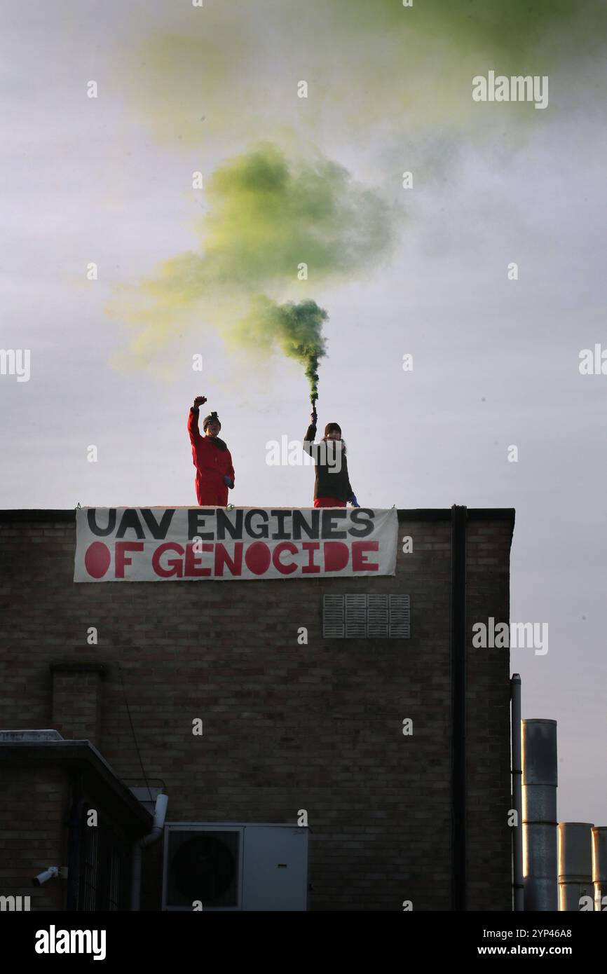 Shenstone, England, Großbritannien. November 2024. Zwei Aktivisten stehen hinter ihrem Banner auf dem Dach und halten farbige Rauchfackeln. Zwei aktionäre von Palestine Action klettern auf das Dach eines benachbarten Unternehmens, um das Dach und die Fenster von UAV-Motoren zu beschädigen und sie in vier Tagen zum dritten Mal abzuschalten. Das Unternehmen, das dem israelischen Waffenhersteller Elbit Systems gehört, stellt Motoren für die Drohnen der Serie Hermes her, die vom israelischen Militär in Gaza und anderswo eingesetzt werden. Palestine Action ist entschlossen, Elbit und seine Partnerunternehmen durch regelmäßige Proteste und direkte Aktionen a unerbittlich ins Visier zu nehmen Stockfoto