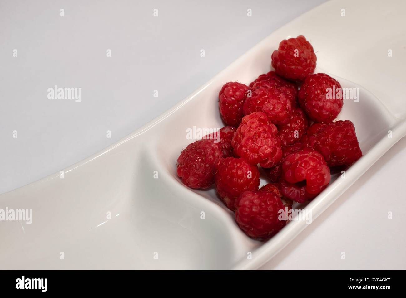 Köstliche reife Himbeeren in einer weißen Schale auf hellem Hintergrund mit Kopierraum Stockfoto