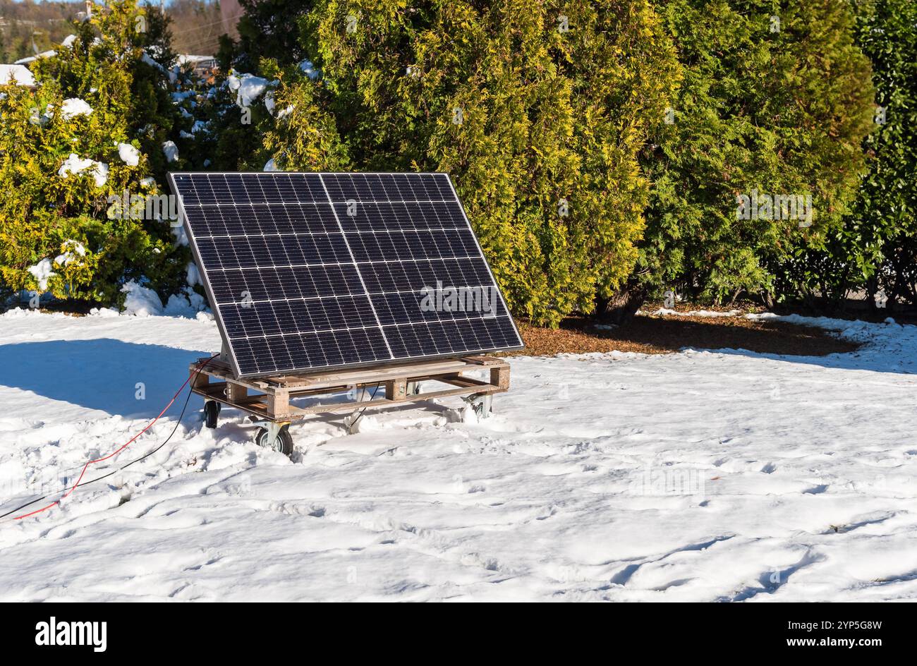 Photovoltaikpaneel auf einer Holzpalette im verschneiten Garten im Winter. Konzept der grünen Energie. Stockfoto