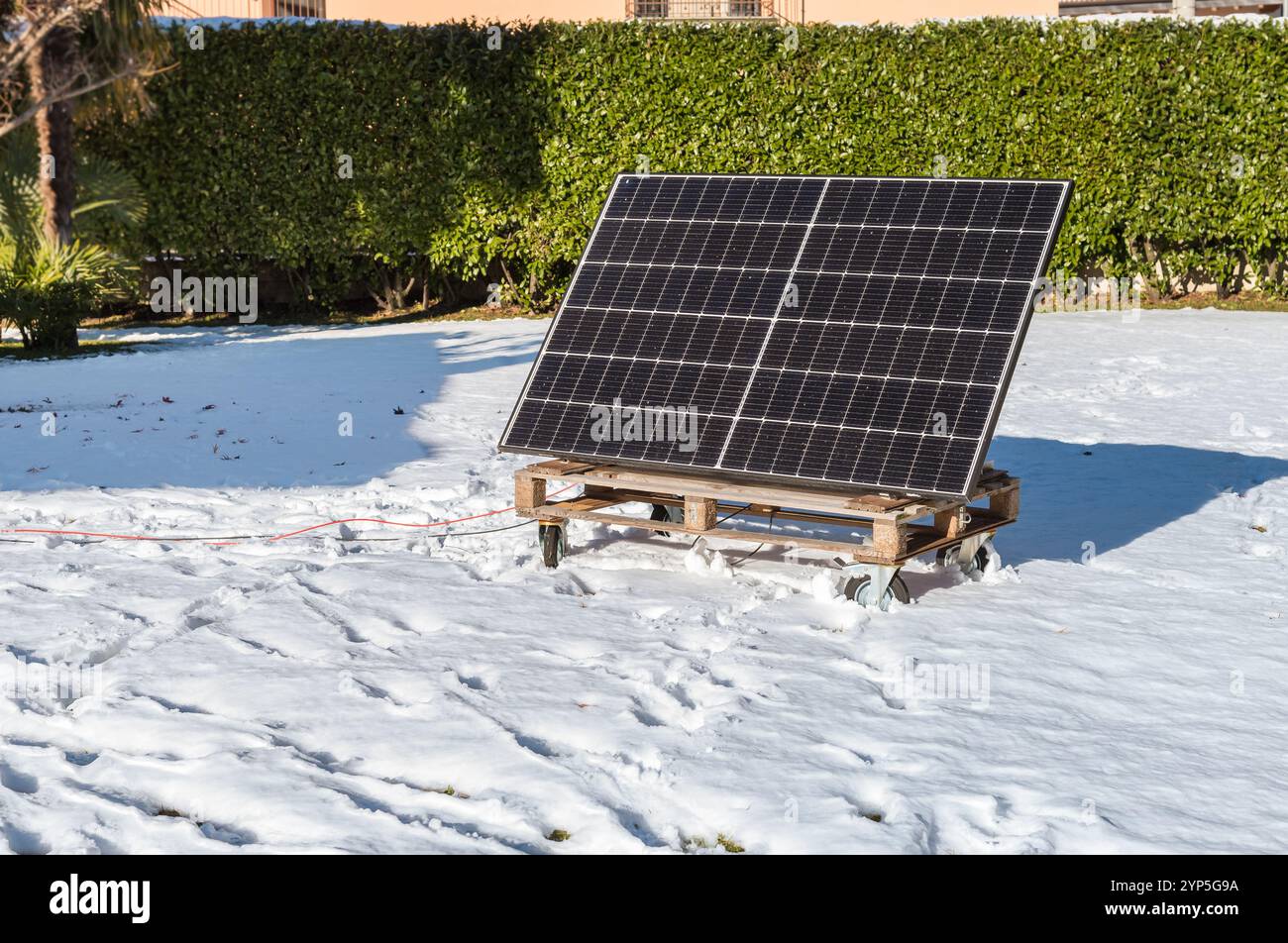 Photovoltaikpaneel auf einer Holzpalette im verschneiten Garten im Winter. Konzept der grünen Energie. Stockfoto