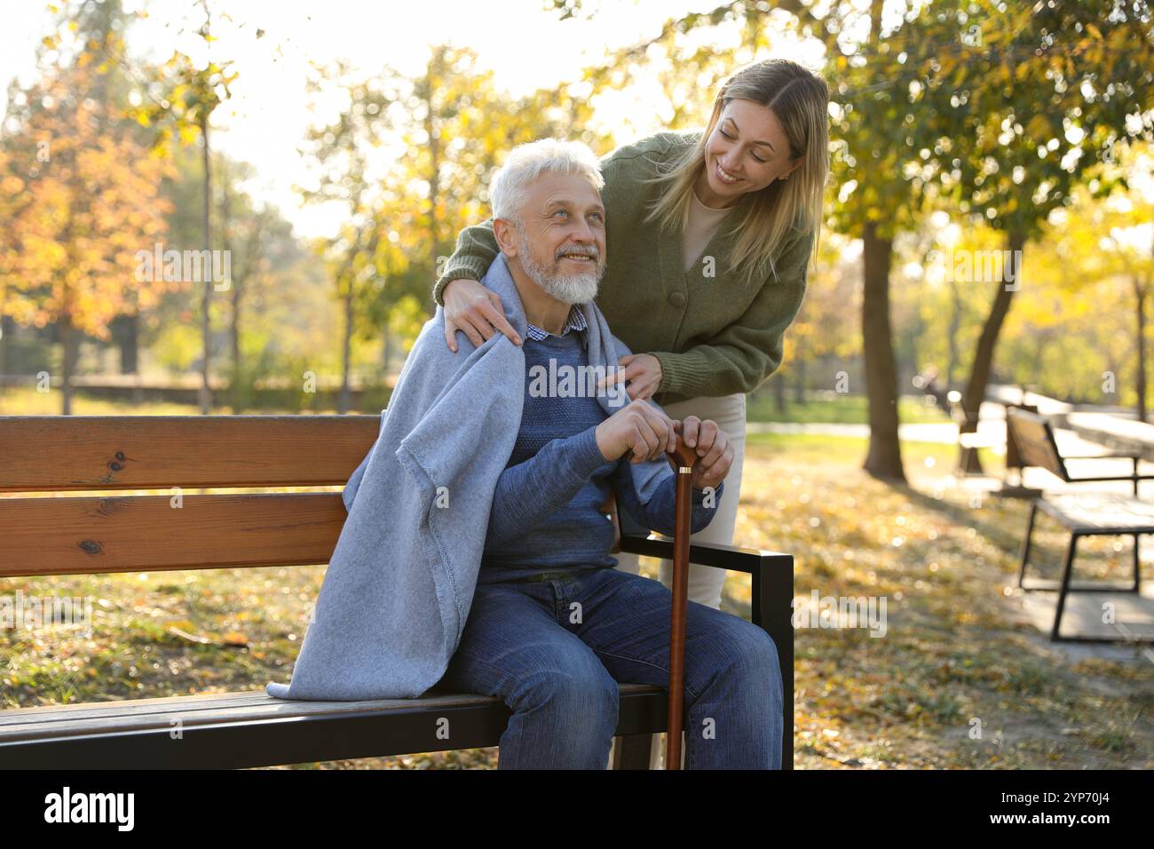 Betreuer, der Senioren auf Holzbank im Park hilft. Häuslicher Gesundheitsdienst Stockfoto
