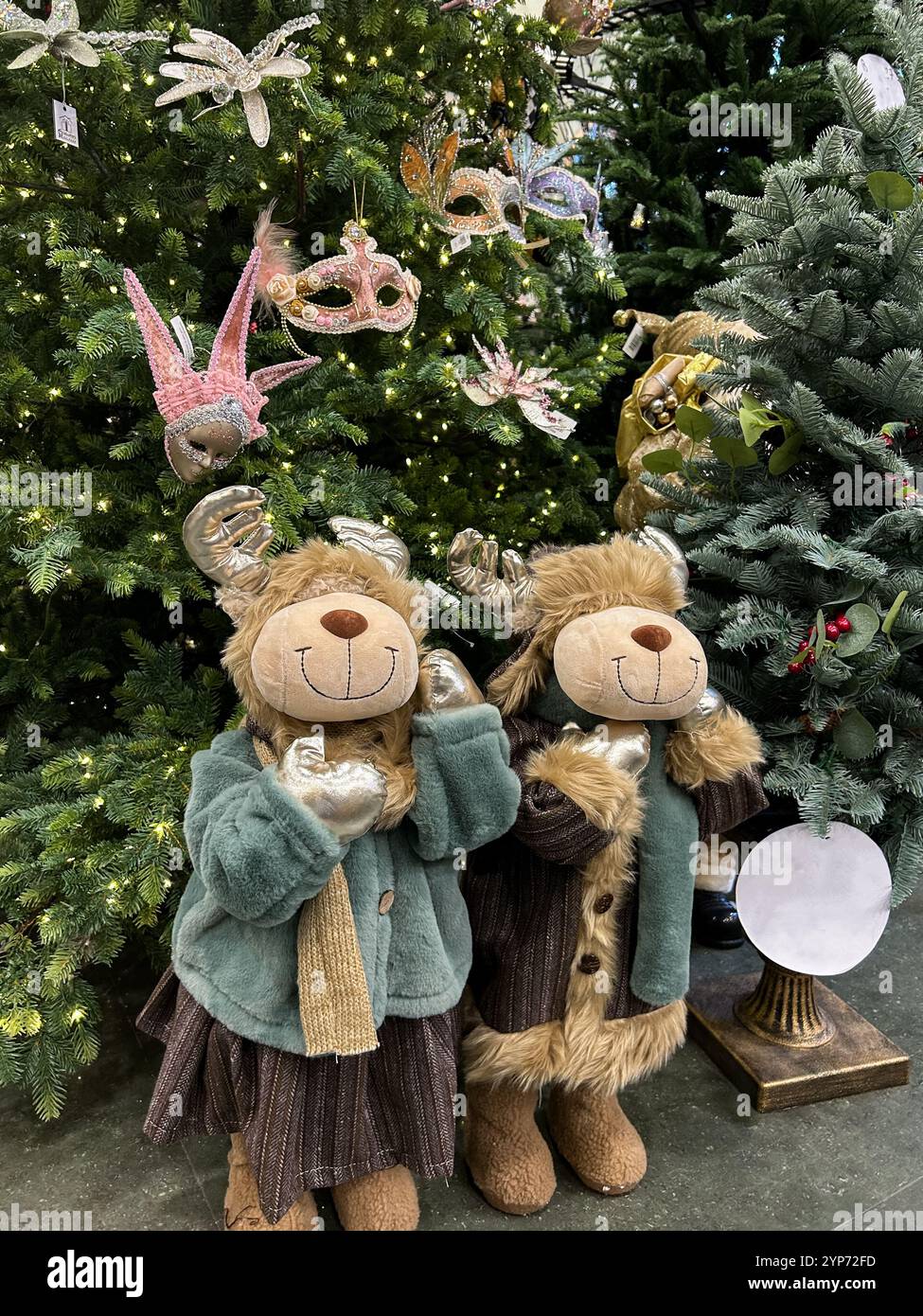 Dieses vertikal ausgerichtete Foto zeigt eine festliche Winterszene mit zwei fröhlichen gefüllten Rentierfiguren in warmen und stilvollen Outfits. Ein Stockfoto