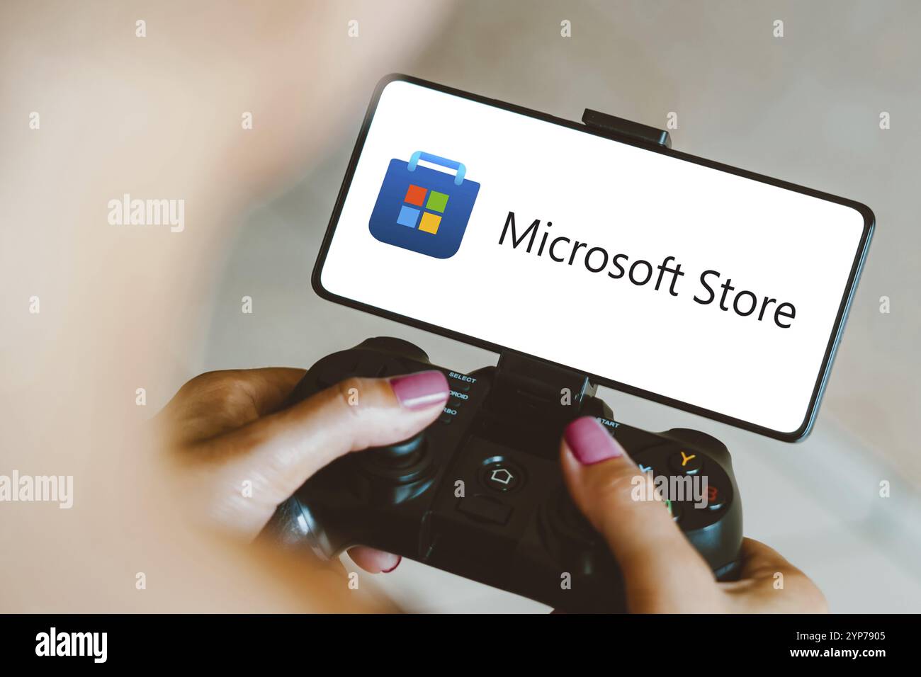 In dieser Fotoabbildung wird das Microsoft Store-Logo auf einem Smartphone-Bildschirm angezeigt, während eine Person auf einem Gaming-Gamepad spielt Stockfoto