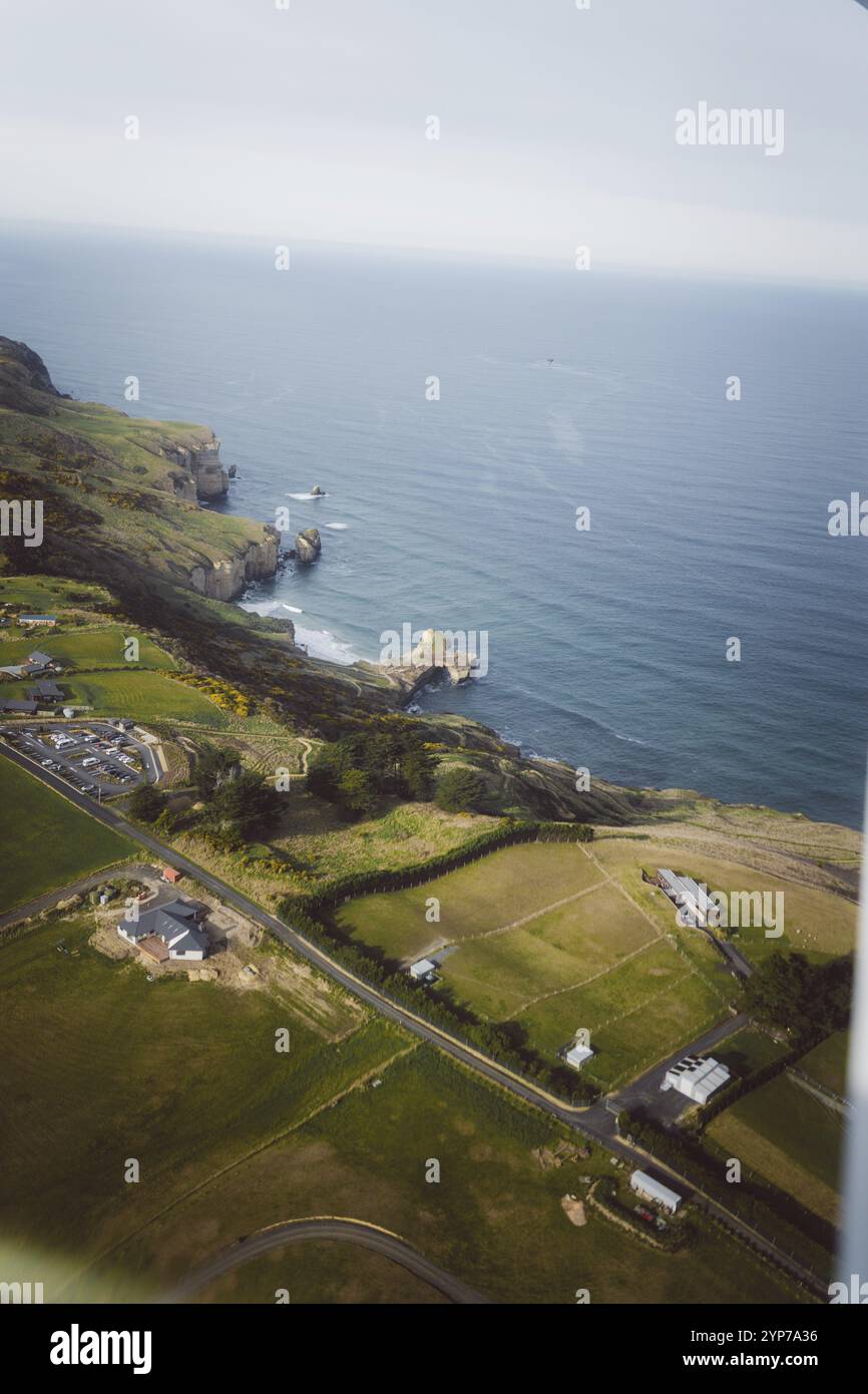 Ländliche Häuser und grüne Felder erstrecken sich bis zu einer fernen Klippenküste, Dunedin, Neuseeland, Ozeanien Stockfoto