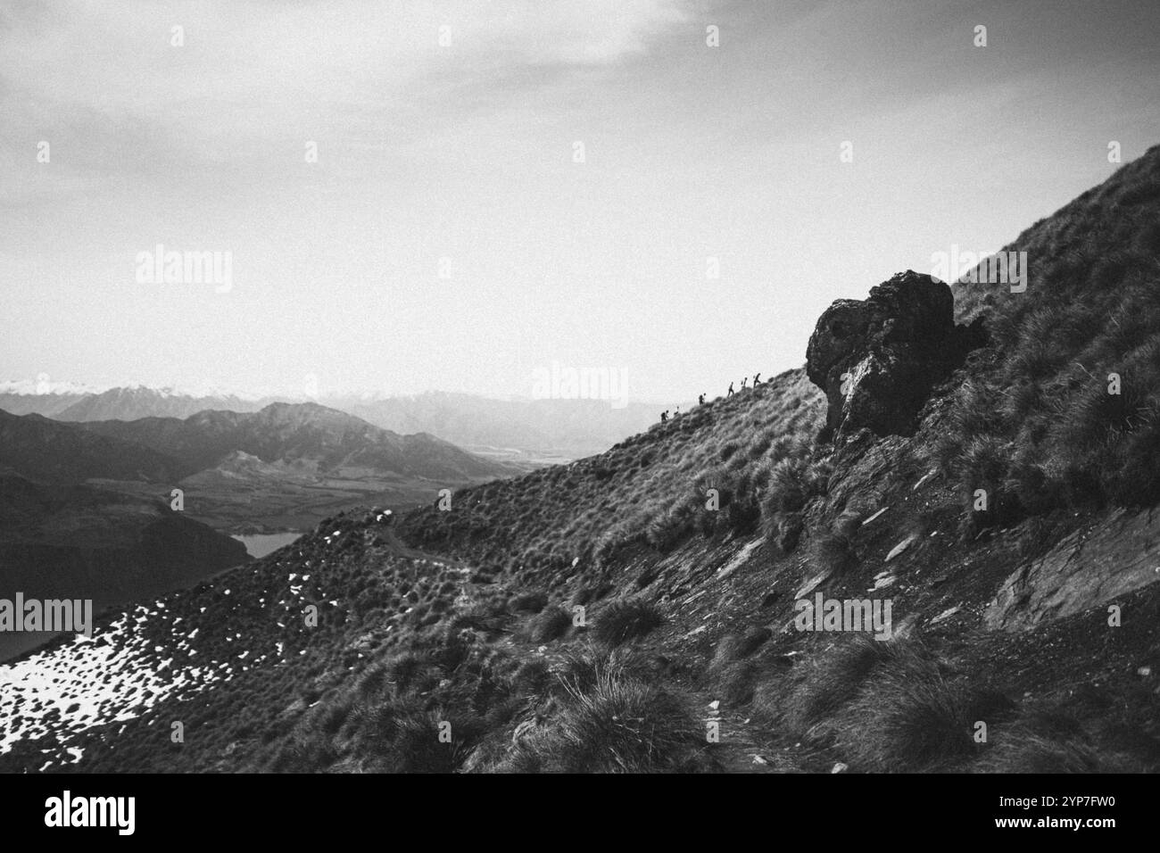 Ein steiniger Pfad schlängelt sich durch eine schwarz-weiße Berglandschaft, gesäumt von Gras und Felsen, Roys Peak, Wanaka, Neuseeland, Ozeanien Stockfoto