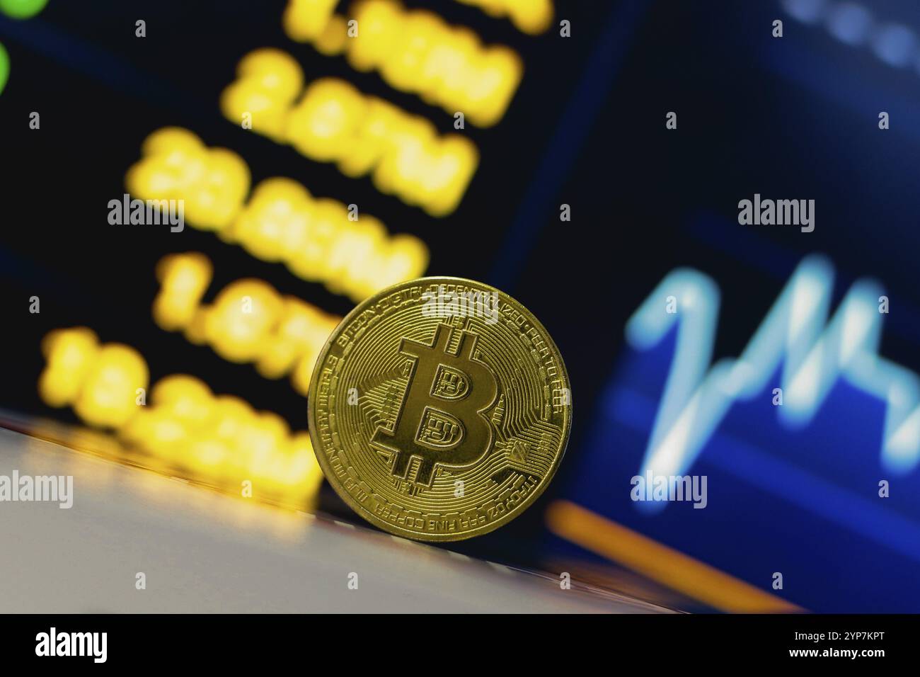 In dieser Abbildung ist eine Bitcoin-Münze auf dem Tisch und im Hintergrund ein Börsendiagramm zu sehen Stockfoto