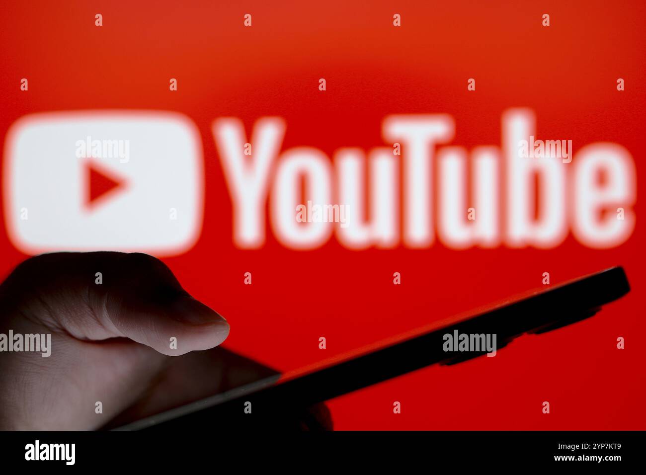 In dieser Fotoabbildung ist das YouTube-Logo im Hintergrund einer Silhouette zu sehen, die Personen mit einem Smartphone hält Stockfoto