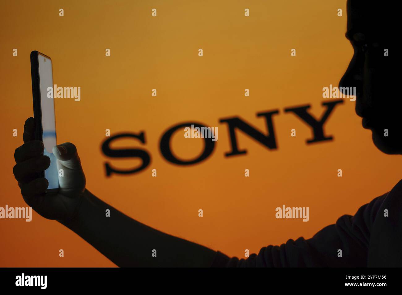 In dieser Fotoabbildung ist das Sony Logo im Hintergrund einer Silhouette einer Frau zu sehen, die ein Mobiltelefon hält Stockfoto