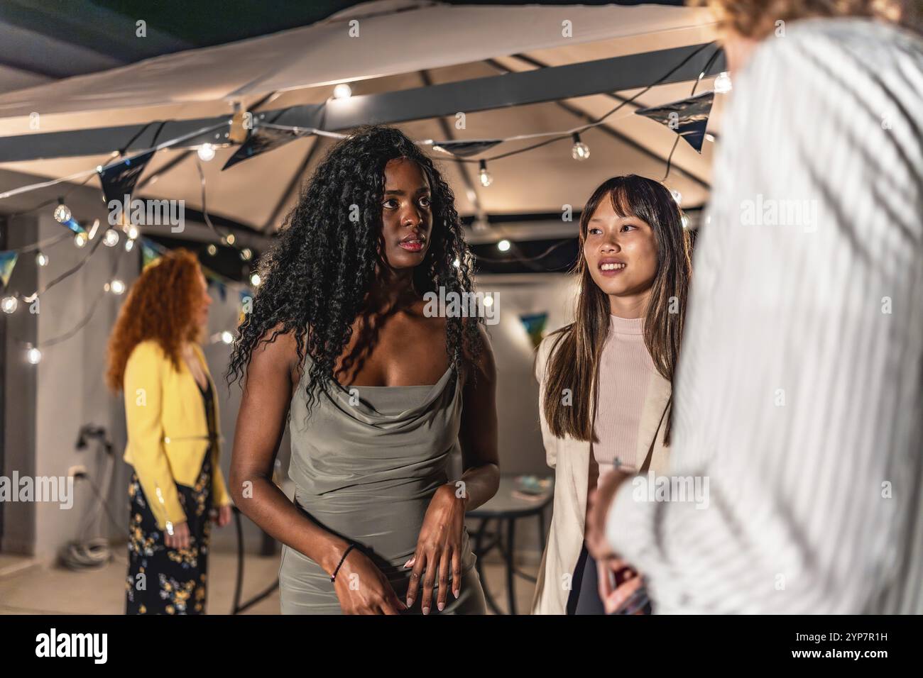 Multiethnische Feinde kleiden elegante Kleidung und unterhalten sich ruhig während der Abendparty auf der Terrasse Stockfoto