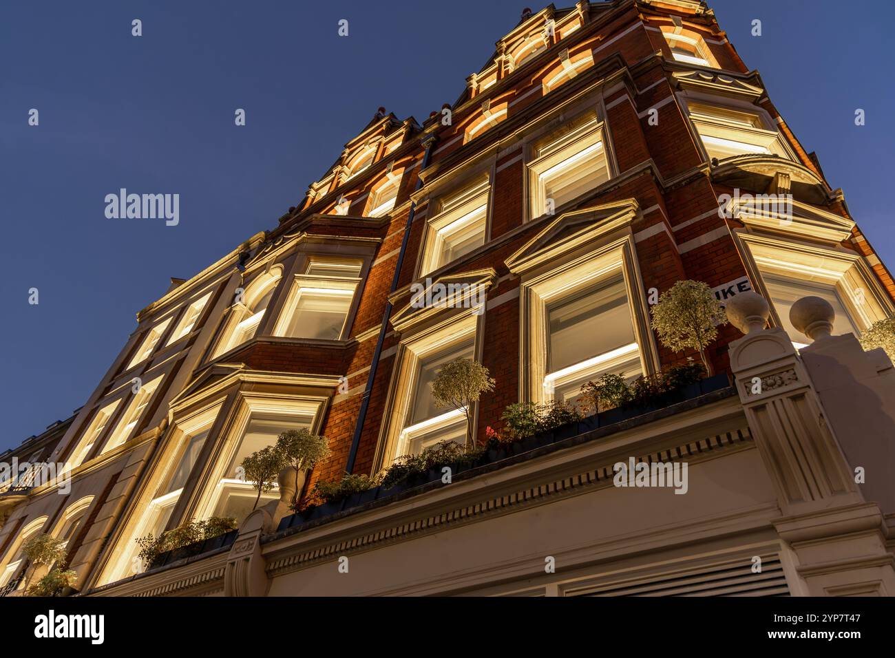 Klassische Londoner Architektur mit warmer Beleuchtung bei Nacht, mit kunstvollen Designdetails und einer Fassade aus rotem Backstein. Stockfoto