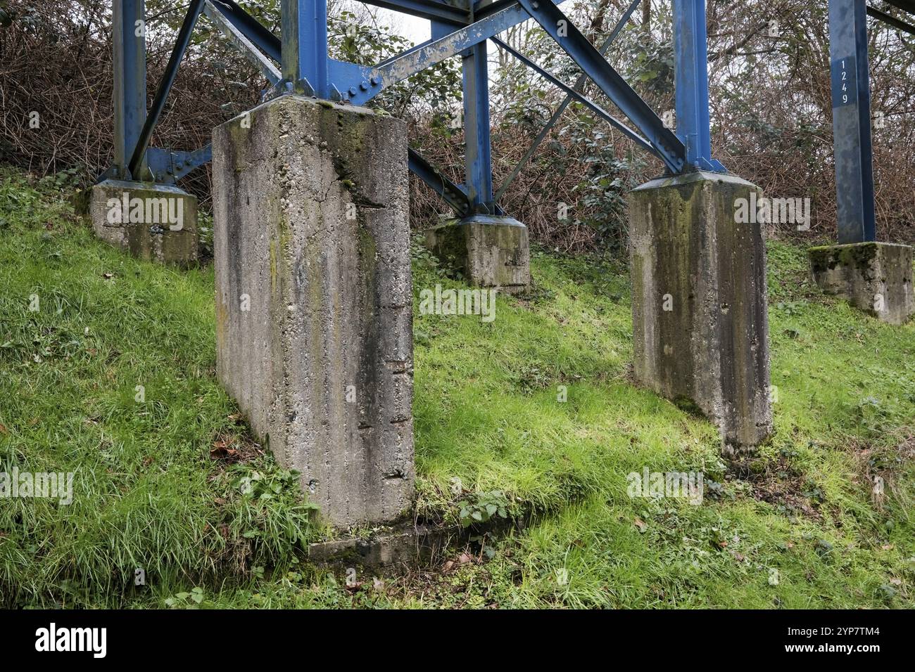 Industrielle Stützkonstruktion mit blauen Metallträgern, die in Betonsockeln im grünen Gras verankert sind Stockfoto