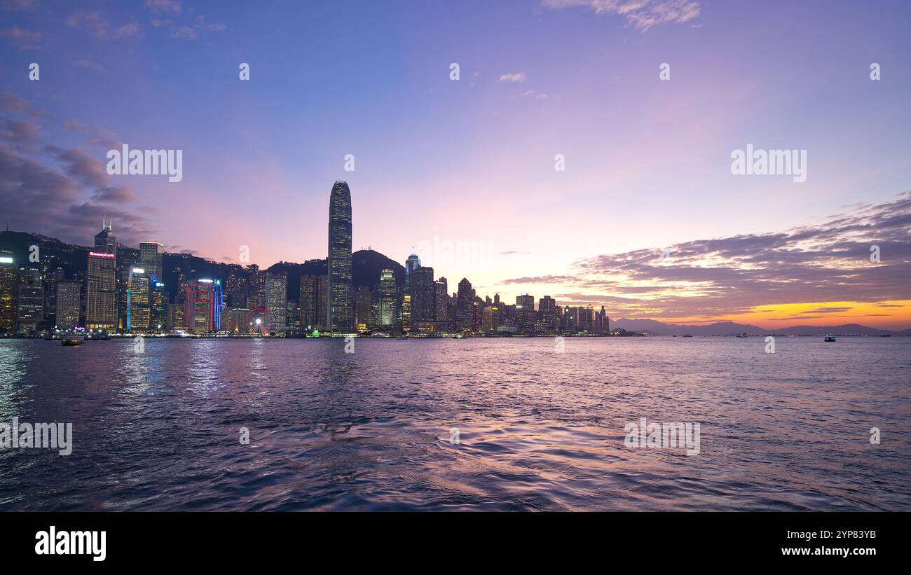 Die Skyline im Zentrum von Hongkong bei Sonnenuntergang mit violettem und orangefarbenem Himmel über dem Victoria Harbour. Hongkong - 25. Oktober 2024 Stockfoto