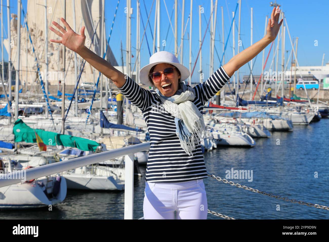 Eine Frau mittleren Alters in guter Laune im marineblauen Stil hat Spaß im Hintergrund der Bucht mit Yachten Stockfoto