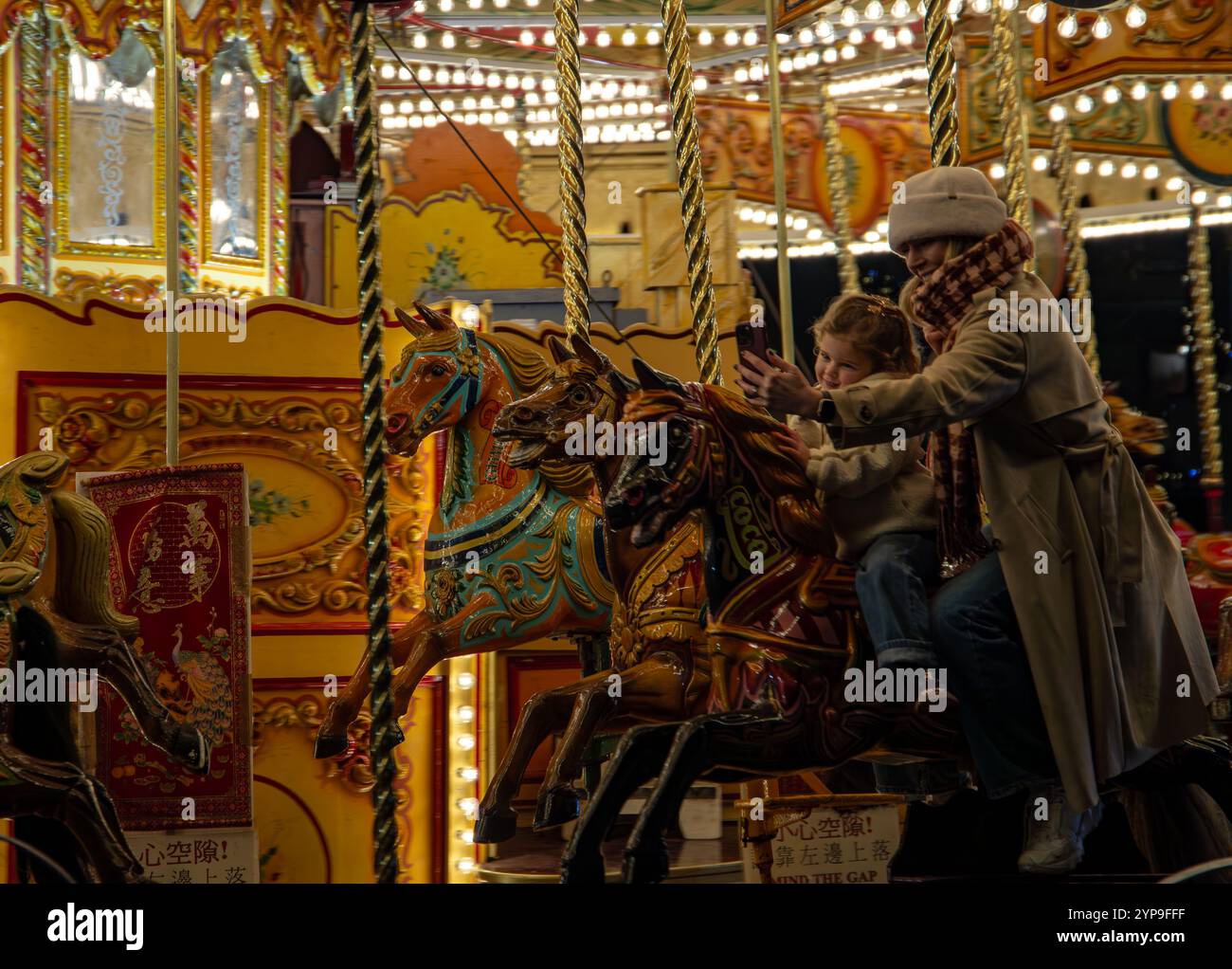 Kind und Eltern genießen eine magische Fahrt auf einem hell beleuchteten Karussell während einer festlichen Abendfeier in York Christmas Market 2024 Stockfoto