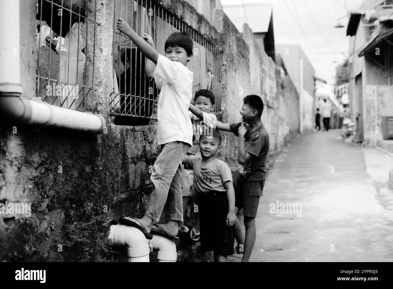 Bogor, 24. November 2024. Vier kleine Kinder stehen zusammen in einer engen Gasse, lächeln und schauen sich in einer lebhaften Umgebung um Stockfoto