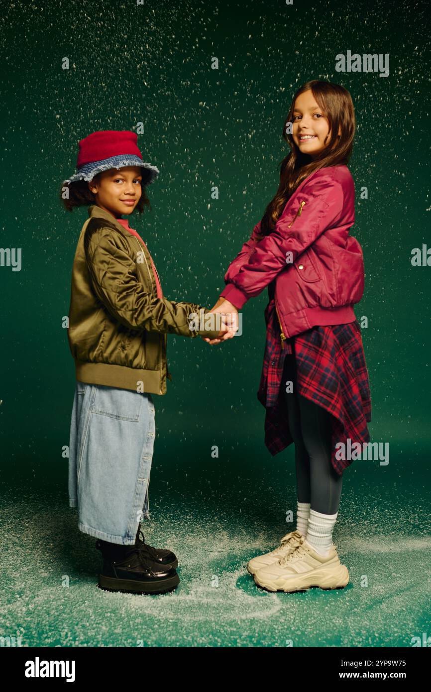 Zwei kleine Mädchen begrüßen die Freude an Weihnachten im Jahr 2025, halten Hände und lächeln zusammen. Stockfoto