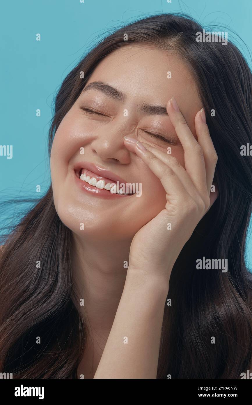 Fröhliche und verspielte junge asiatische Frau mit einer gesunden, sauberen Haut berührend auf sich selbst Gesicht und Glück Lächeln, vertikale Nahaufnahme Foto. Stockfoto