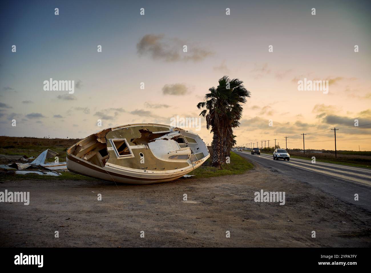Ein Boot liegt umgekippt neben einer Straße, während Fahrzeuge vorbeifahren. Stockfoto