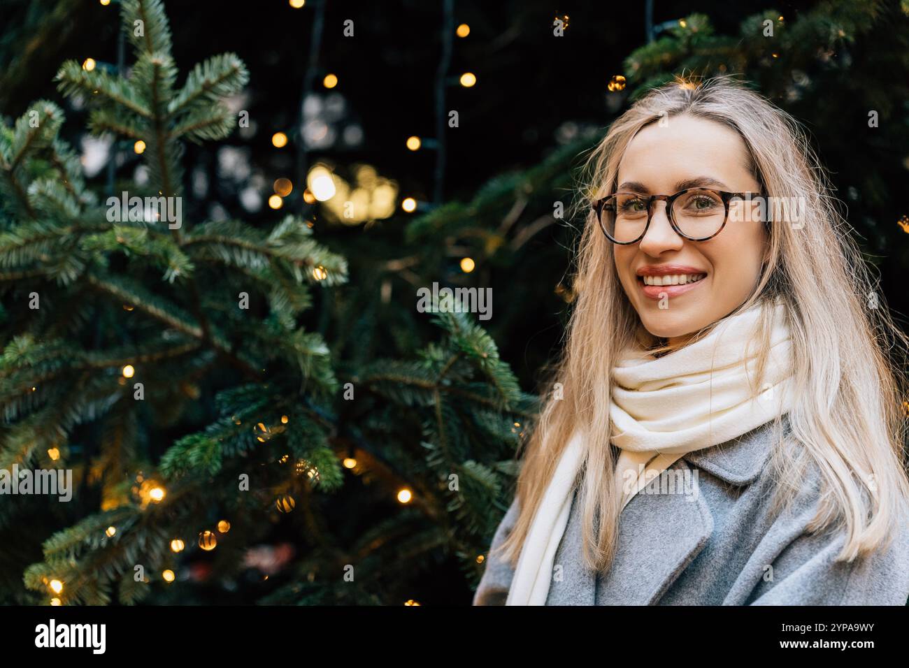 Junge Frau in Brille vor dem Weihnachtsbaum draußen Stockfoto