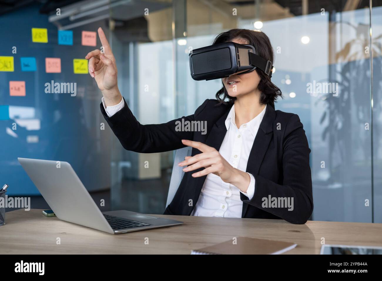 Geschäftsfrau, die ein Virtual-Reality-Headset trägt, nutzt interaktive digitale Präsentationen. Mithilfe von VR-Technologie erkundet sie immersive Arbeitsplatzlösungen am Schreibtisch. Stockfoto