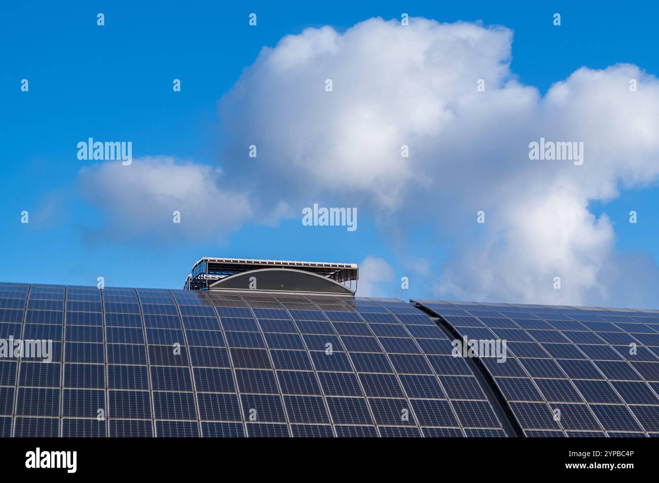 Gekrümmte Solarpaneele, die auf einem Dach installiert sind, erzeugen unter einem bewölkten blauen Himmel saubere Energie und zeigen nachhaltige Energiepraktiken Stockfoto