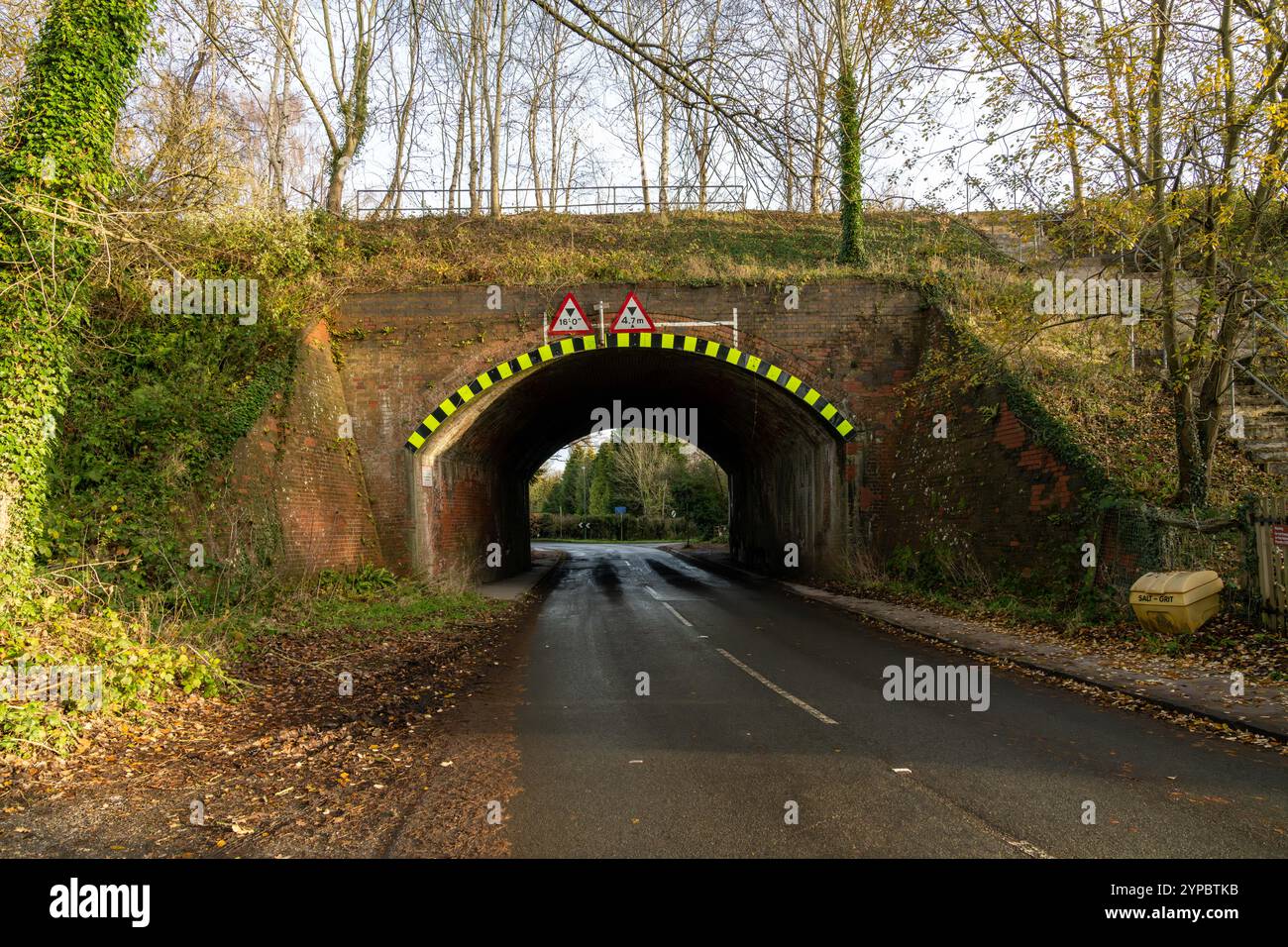 Warnschilder und Höhenbegrenzungszeichen über einem schmalen Straßentunnel unter einer Eisenbahnbrücke im Herbst Stockfoto