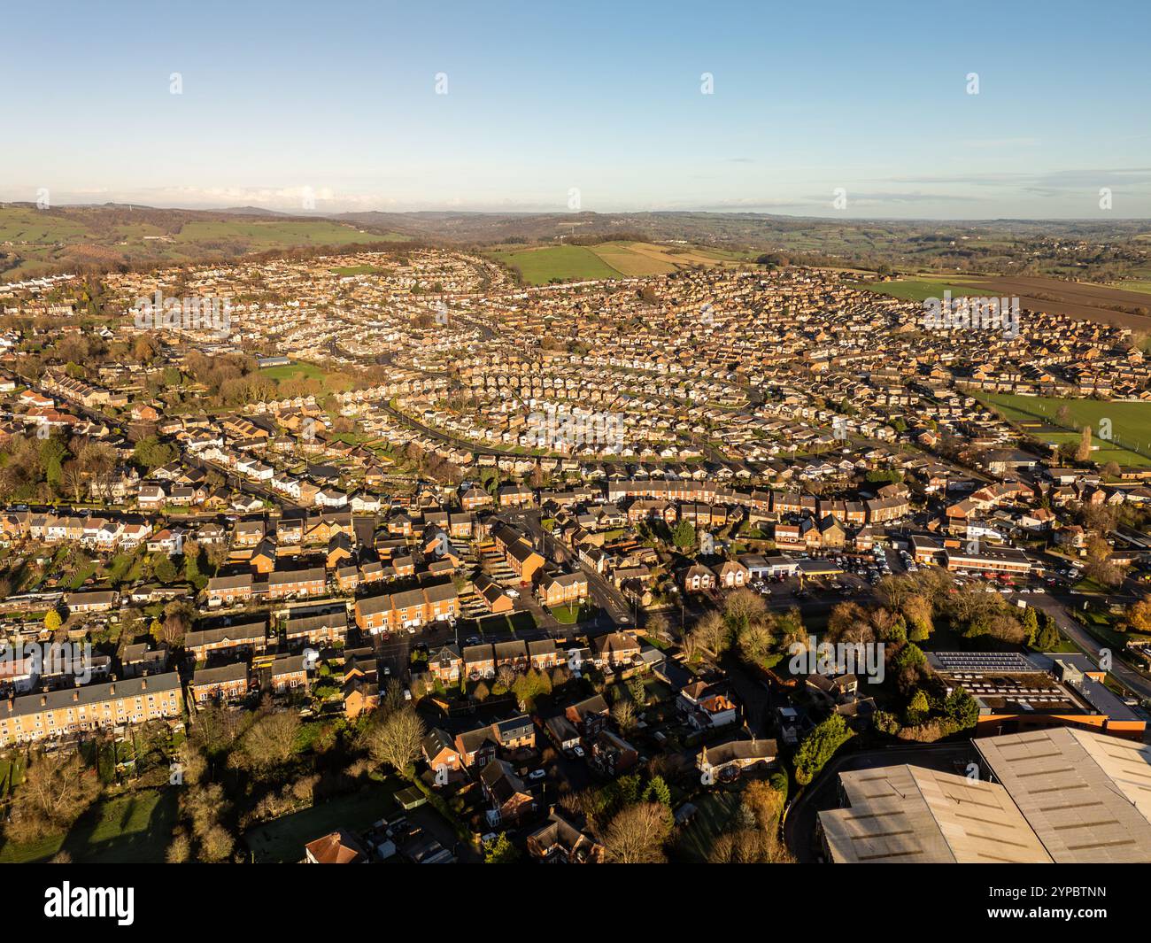 Aus der Vogelperspektive einer vorstädtischen Wohnsiedlung, die sich in die umliegende Landschaft ausdehnt und im warmen Glanz des Sonnenuntergangs getaucht ist Stockfoto