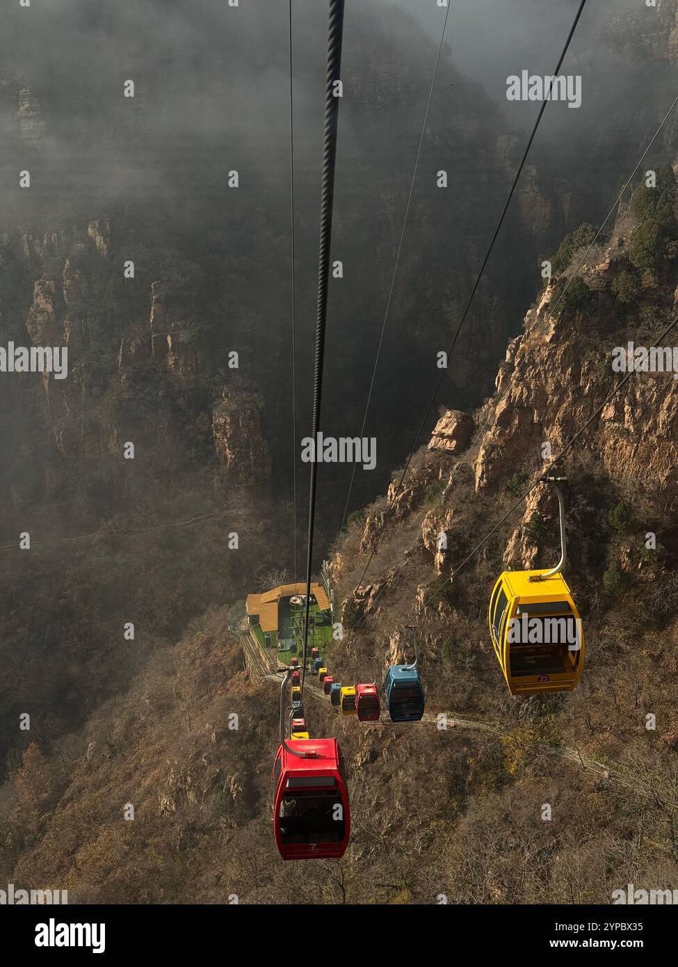 Seilbahnen, die Menschen hoch oben auf einem Berg transportieren, während der Nebel durch die Gipfel steigt. - Smartphone-aufgenommenes Stockfoto