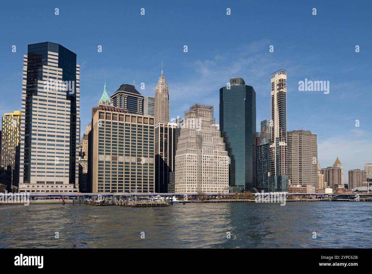 Hohe Gebäude säumen das Wasser und bieten eine Mischung aus moderner und klassischer Architektur. Heller Himmel und ruhiges Wasser spiegeln die pulsierende Energie wider. Stockfoto