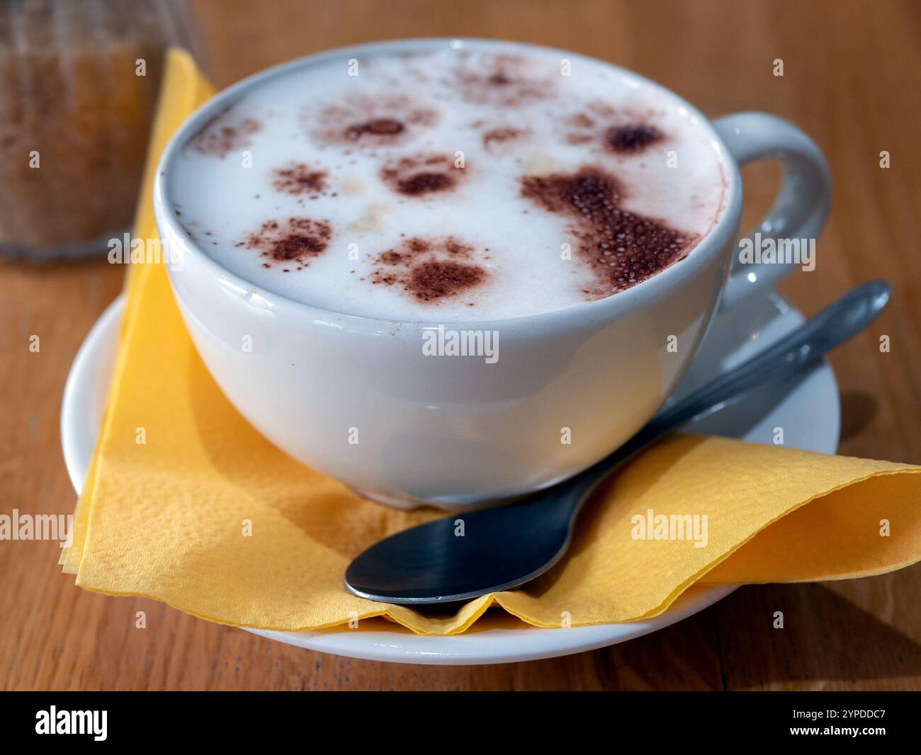 Tallinn, Estland - 16. August 2024: Gelbe Tasse Kaffee in einem Katzencafé. Der Schaum des Getränks zeigt einen Katzen- und Pfotenabdruck, selektiv fokussiert Stockfoto
