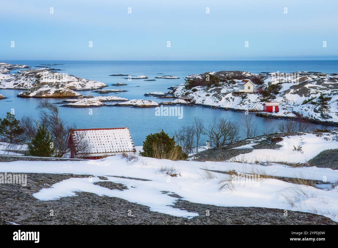 Küstenhütten mit schneebedeckten Dächern, eisigem Gelände und ruhigem blauem Meer. Malerische Szene mit Häusern und gefrorener Landschaft, ideal für Winterfreunde Stockfoto