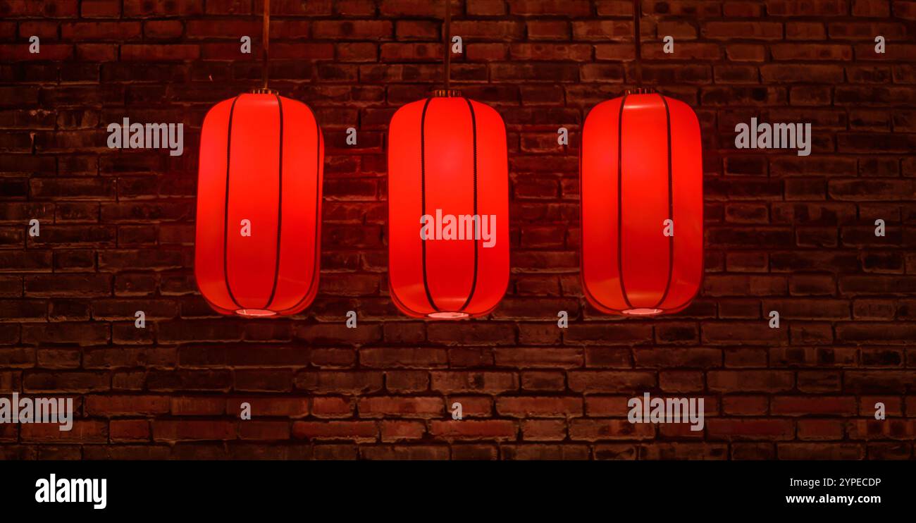 Drei rote chinesische Laternen hängen an einer roten Ziegelwand Stockfoto