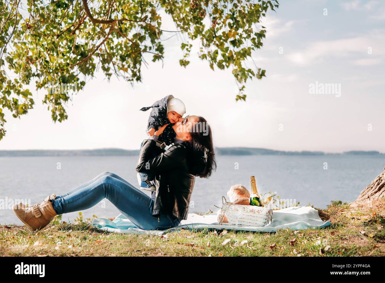 Mutter genießt die schöne Zeit mit ihrem Baby während eines entspannenden Picknicks am See im Schatten eines Baumes Stockfoto