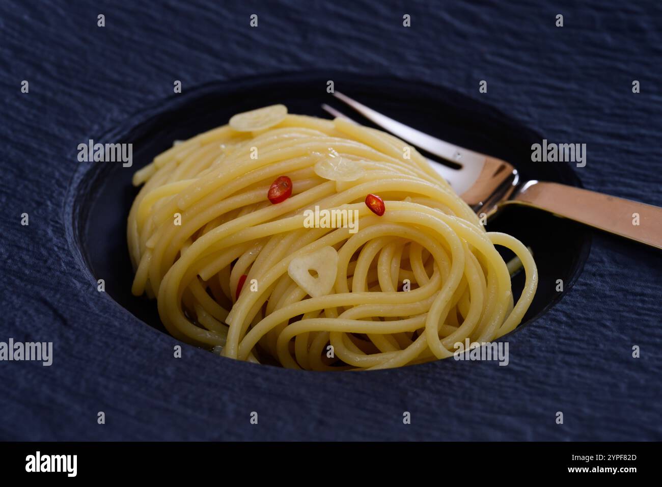 Spaghetti Colatura di Alici mit Knoblauch und Peperoncini auf einer schwarzen Platte Nahaufnahme Stockfoto