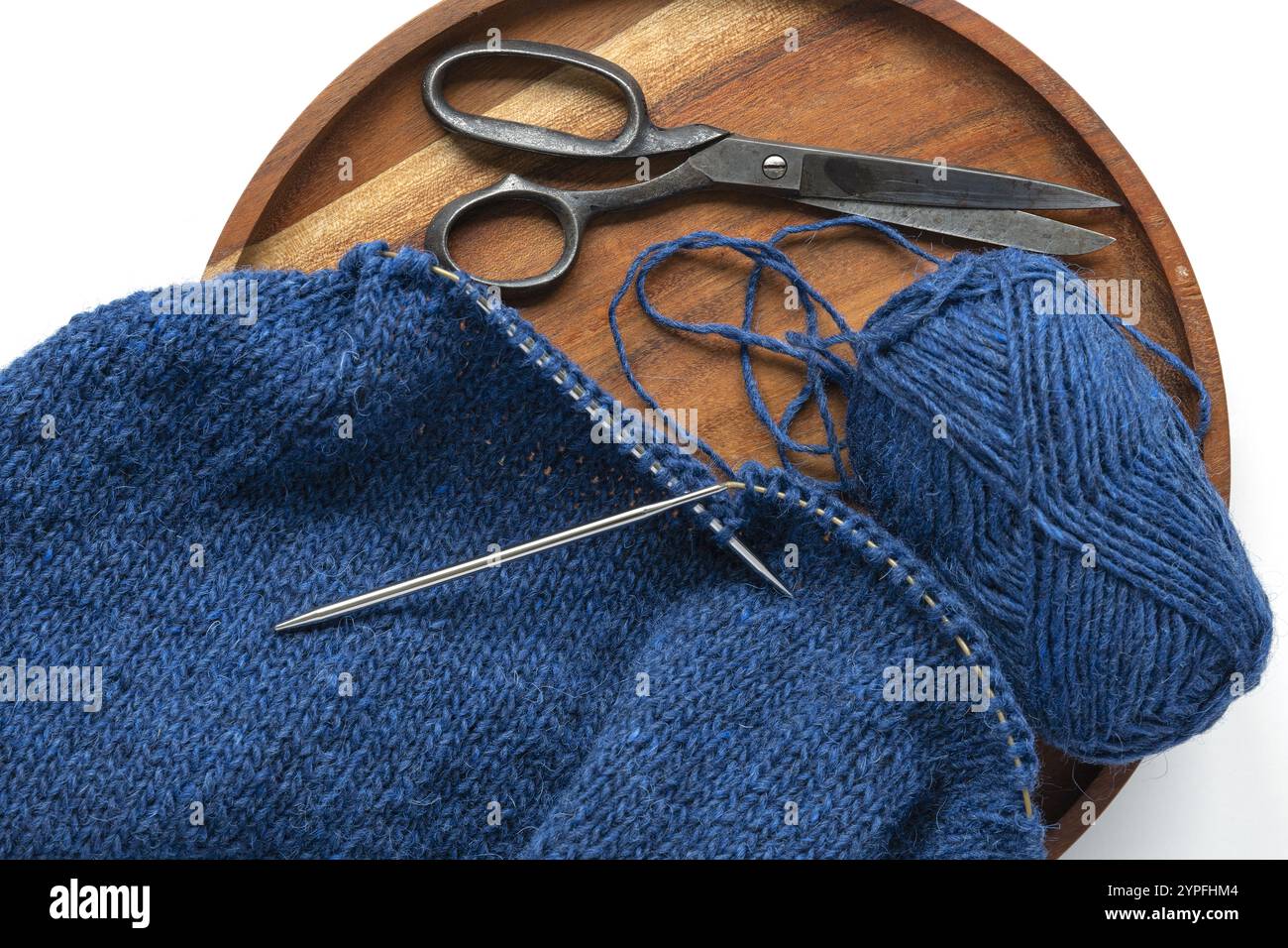 Flachbild-Fotografie eines blauen Wollgarns, das mit Garnkugel und Vintage-Schere auf die Metallnadeln strickt, Stockinette-Naht gestrickte Textur in prog Stockfoto